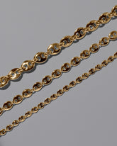 Closeup details of the CRZM Gold Bedrock Mini Necklace, Gold Bedrock Medium Necklace, and Gold Bedrock Necklace on light color background.