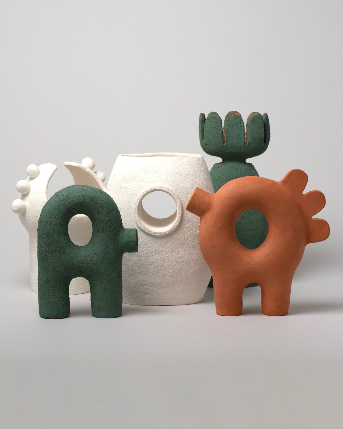 Group photo of Stephanie Phillips Curvature Sculpture, Ferdi Sculpture, Flower Sculpture, White Moon Bulb Sculpture, and Single Barrel Vessel on light color background.