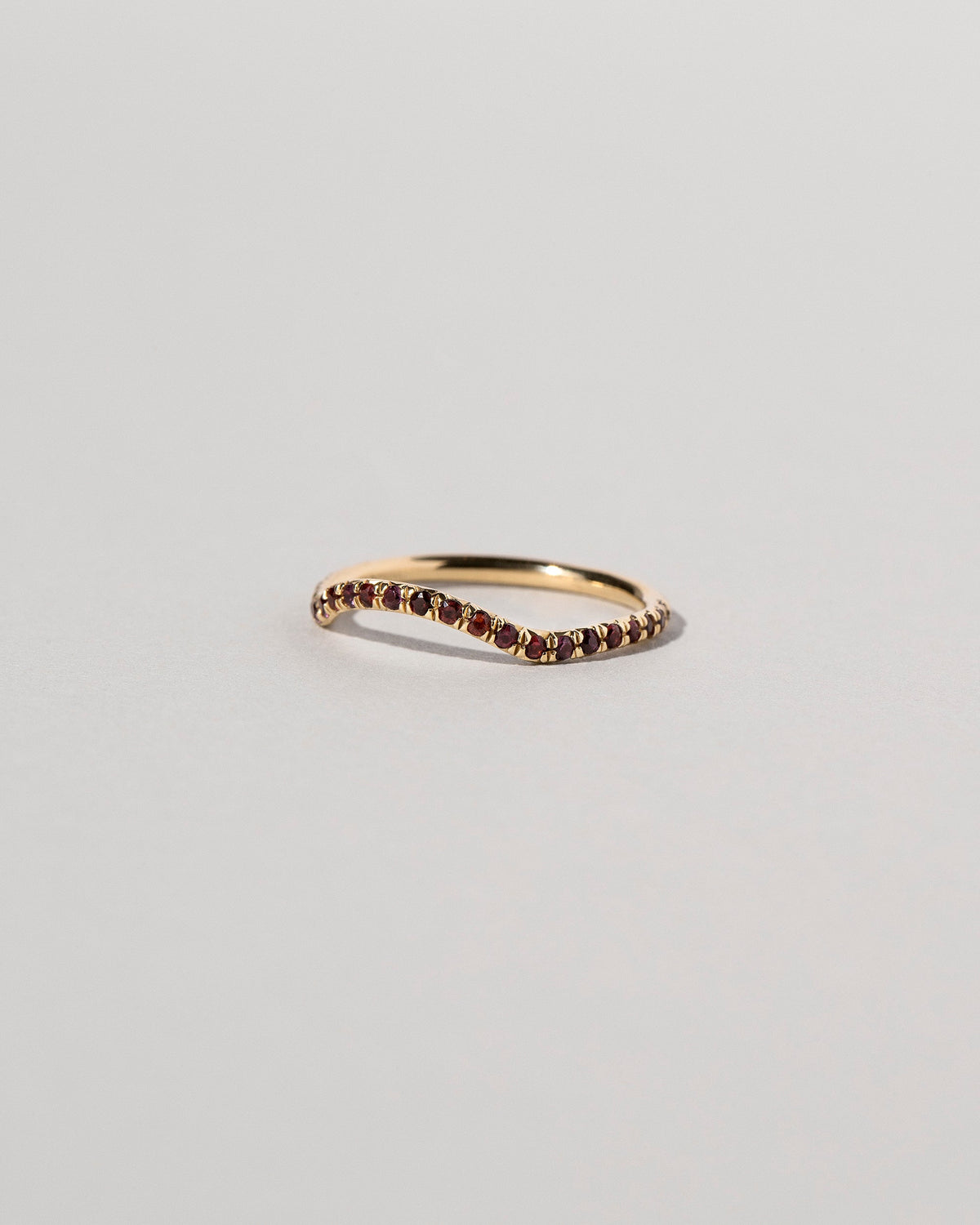 View from the side of the Gold Garnet Pavé Mini Curve Band on light color background.