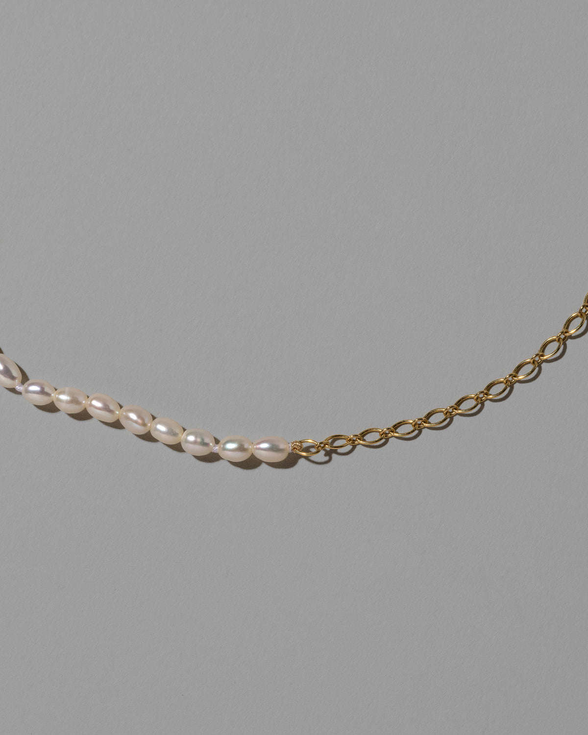 Closeup details of the Half Oval Chain & White Seed Pearl Necklace on light color background.
