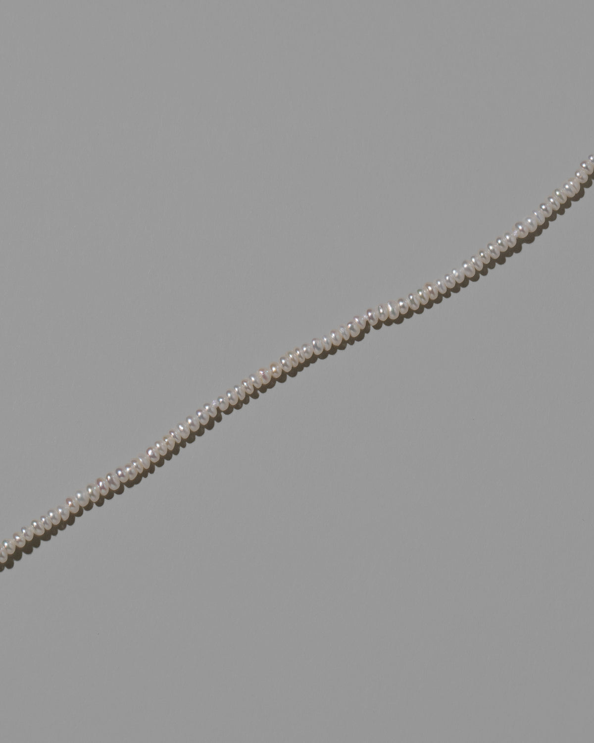 Closeup details of the White Pebble Seed Pearl Anklet on light color background.