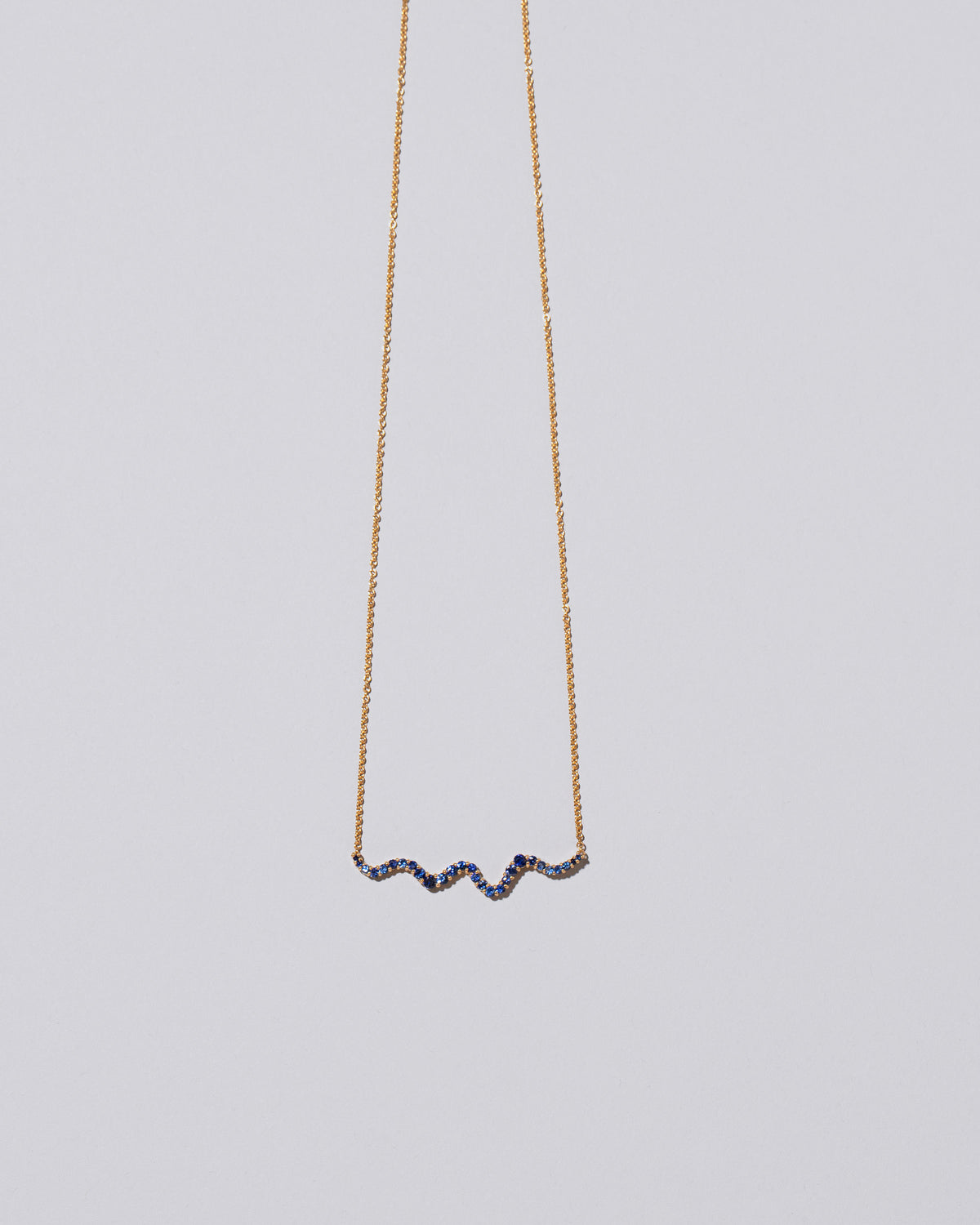 Closeup detail of the Blue Sapphire Ripple Wave Necklace on light color background.