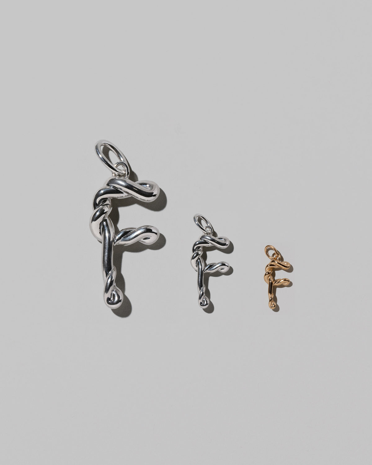 CRZM Large Sterling Silver, Medium Sterling Silver & Mini Letter F Charms set in solid gold on light color background.