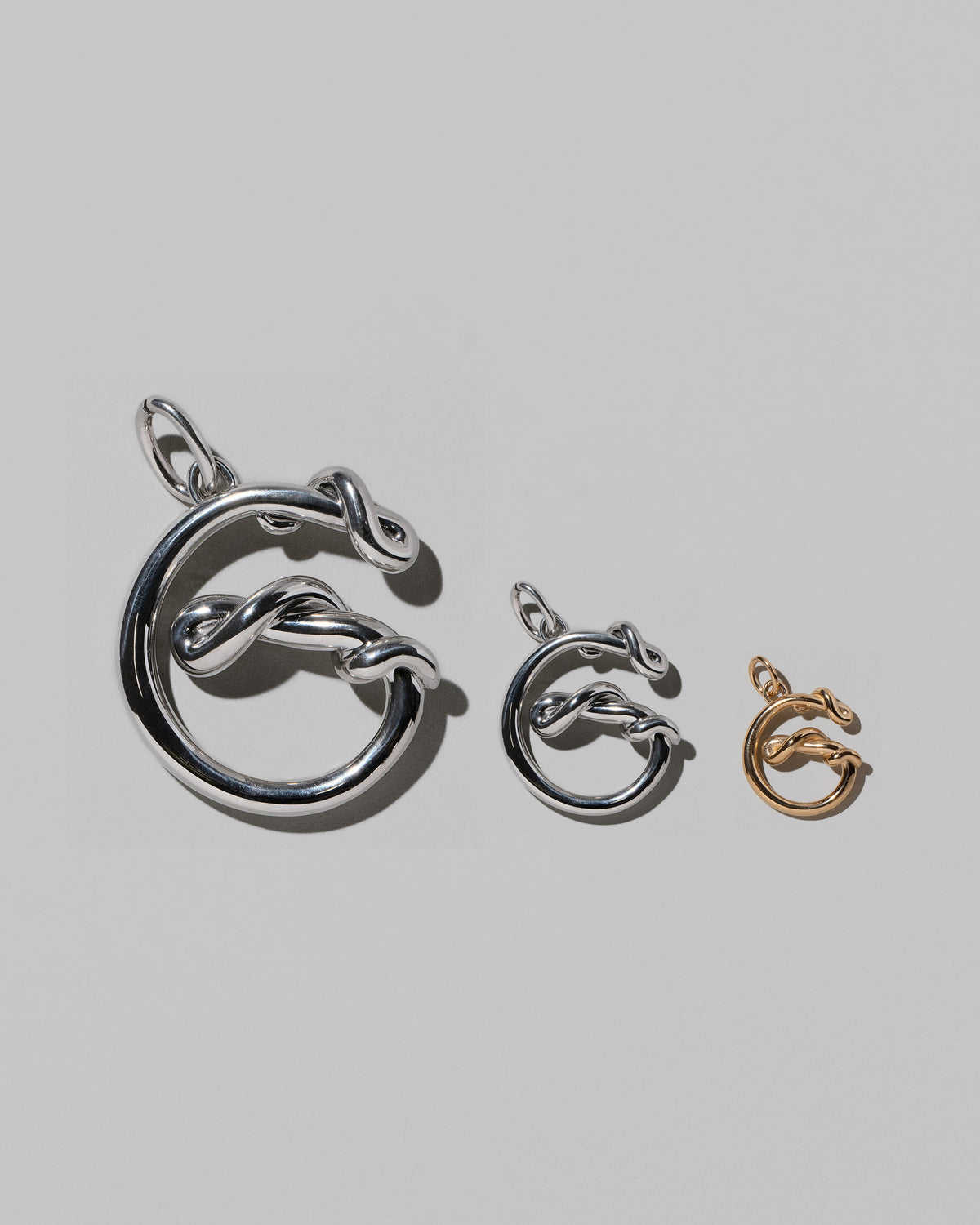 CRZM Large Sterling Silver, Medium Sterling Silver & Mini Letter G Charms set in solid gold on light color background.