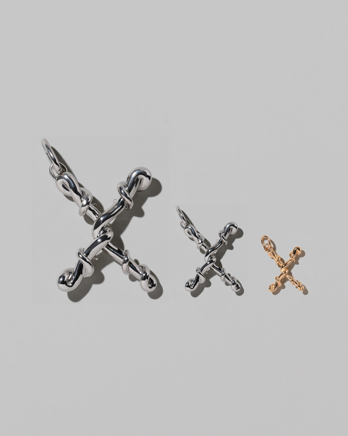 CRZM Large Sterling Silver, Medium Sterling Silver & Mini Letter X Charms set in solid gold on light color background.