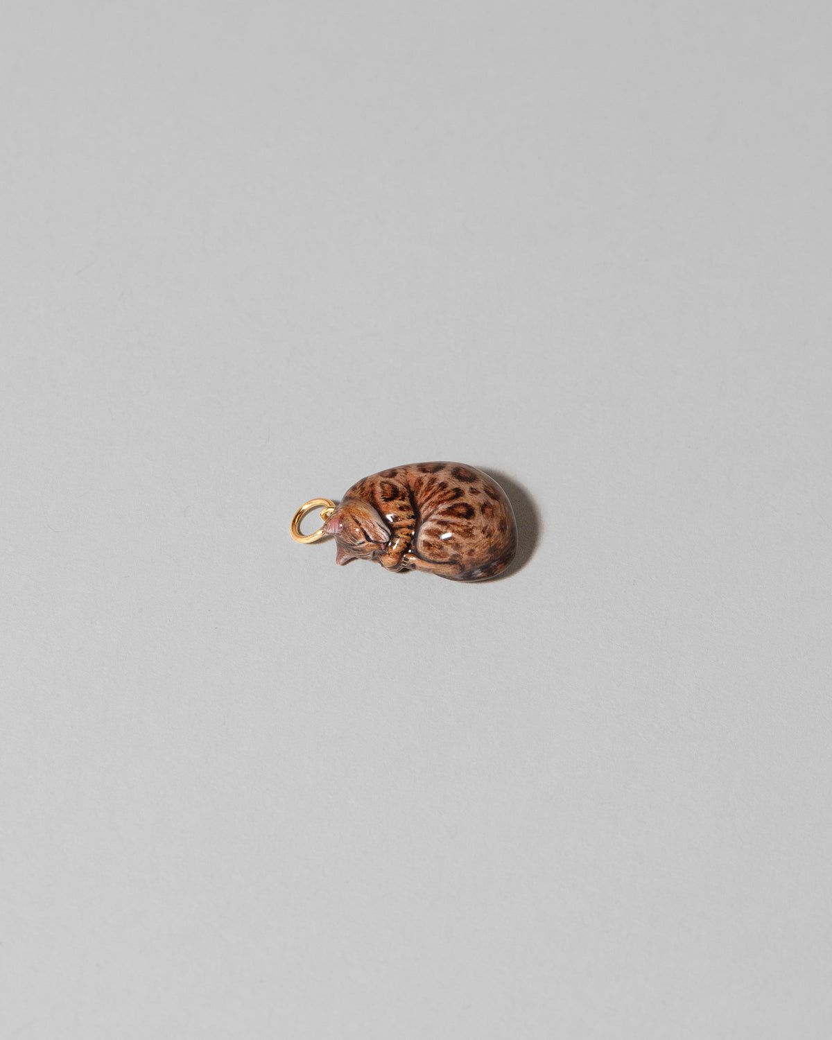 View from the side of the Bengal Curled-Up Cat Charm on light color background.