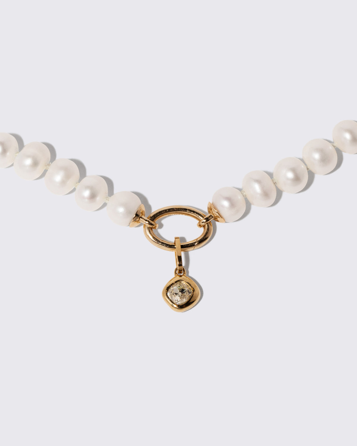 Closeup details of the Diamond Poise Charm and Gold Pearl Openable Link Necklace on light color background.