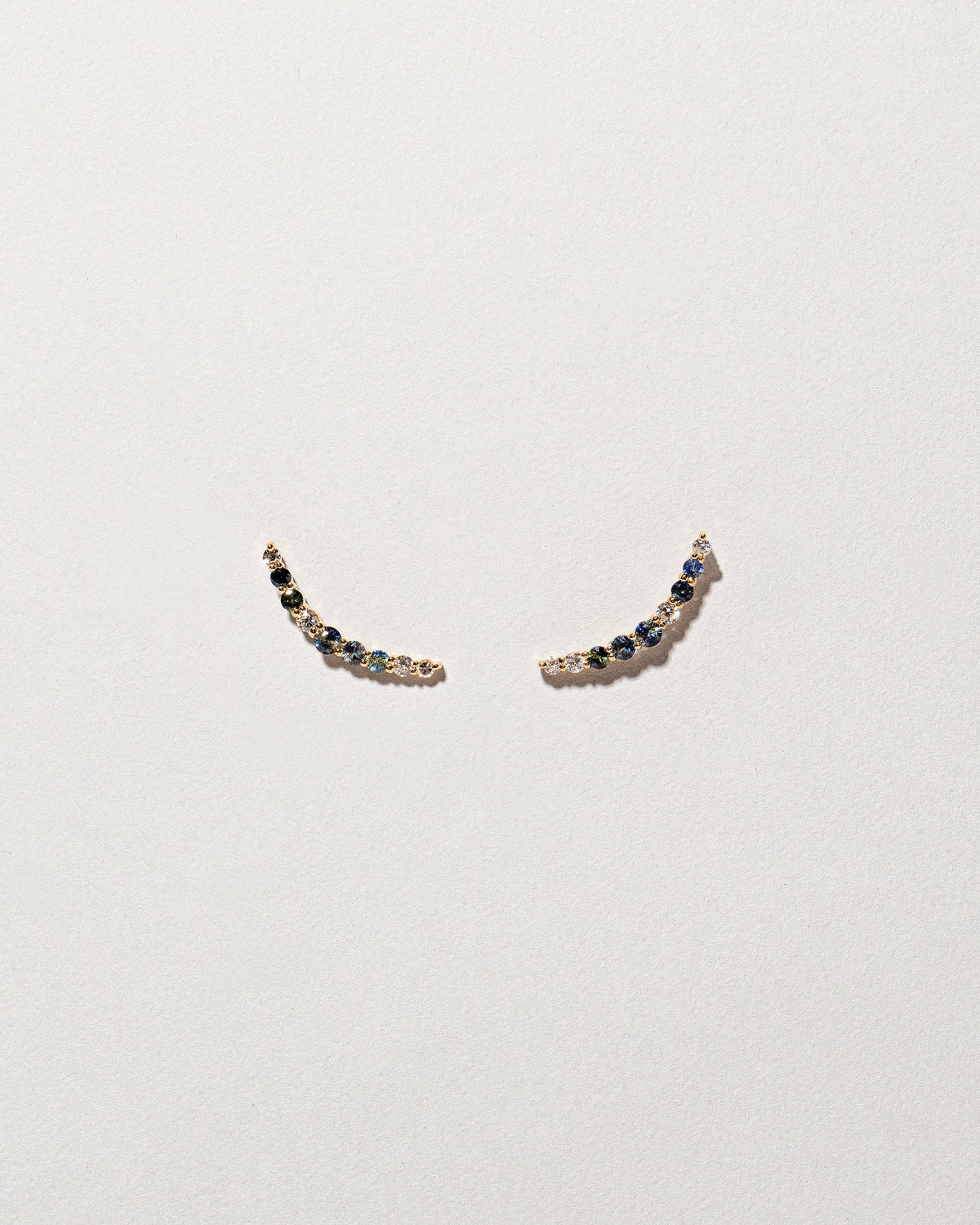 An edition of the Sapphire & White Diamond Crescent Ear Climber Stud Earrings on light colored background.