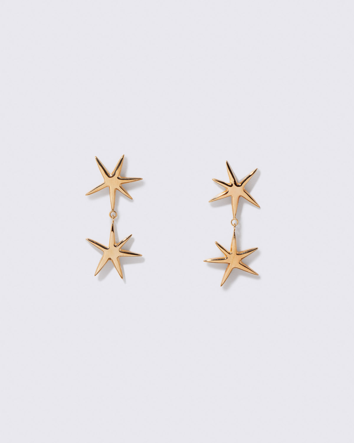 Gold Verve Star Drop Earrings on light color background.