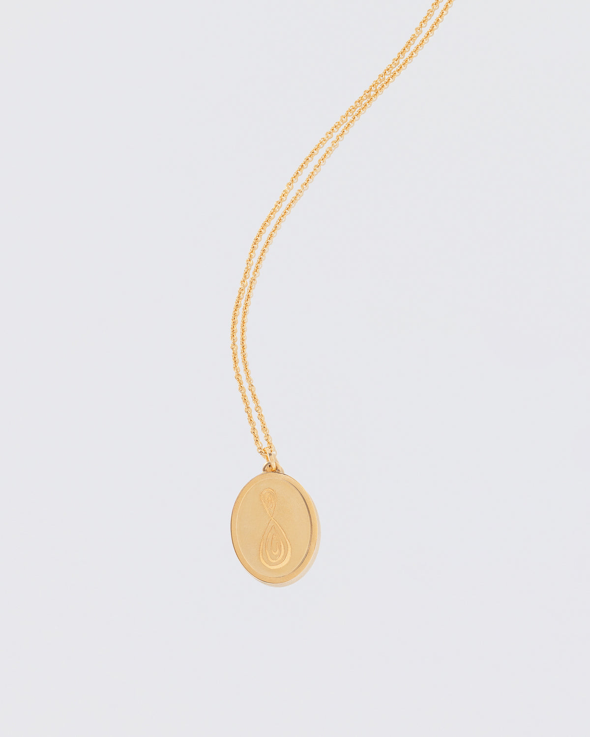 Finished Large Oval Memento Necklace engraved with an abstract symbol on light color background.