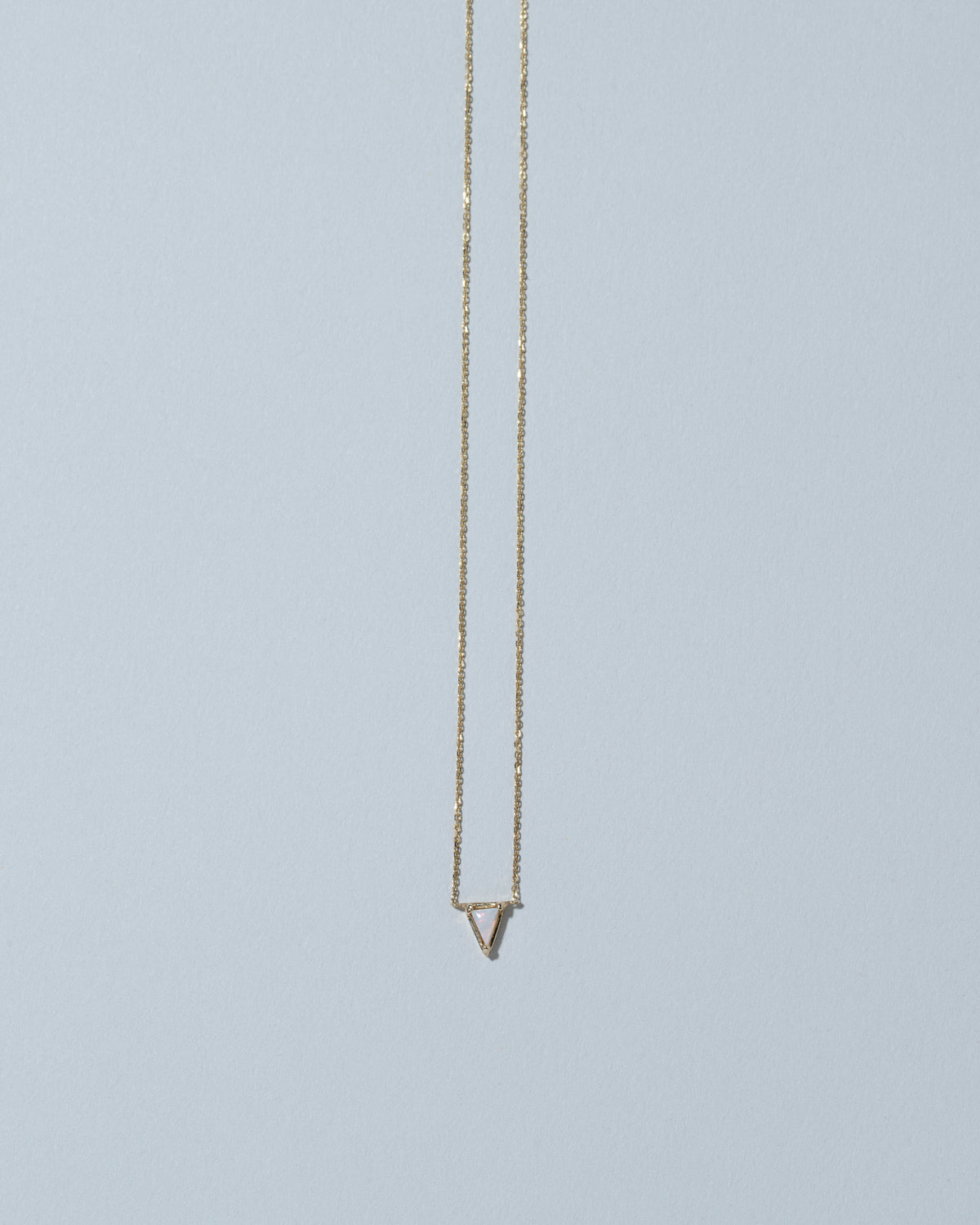 Gold White Opal Triangle Necklace on light color background.