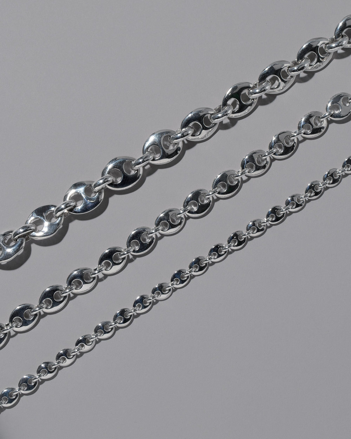 Closeup details of the CRZM Sterling Silver Bedrock Mini Necklace, Sterling Silver Bedrock Medium Necklace, and Sterling Silver Bedrock Necklace on light color background.