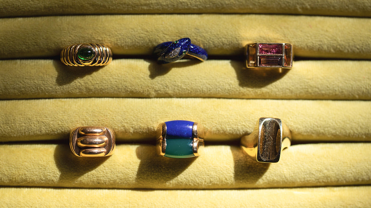 Styled image featuring the Gold Gadroon Ring, Gold Ribbon Ring, Bvlgari Doppio Tronchetto Lapis & Chalcedony Ring, Ribbed Peridot Ring and the Cartier Diamond & Emerald Enamel Snake Ring in green jewelry display.