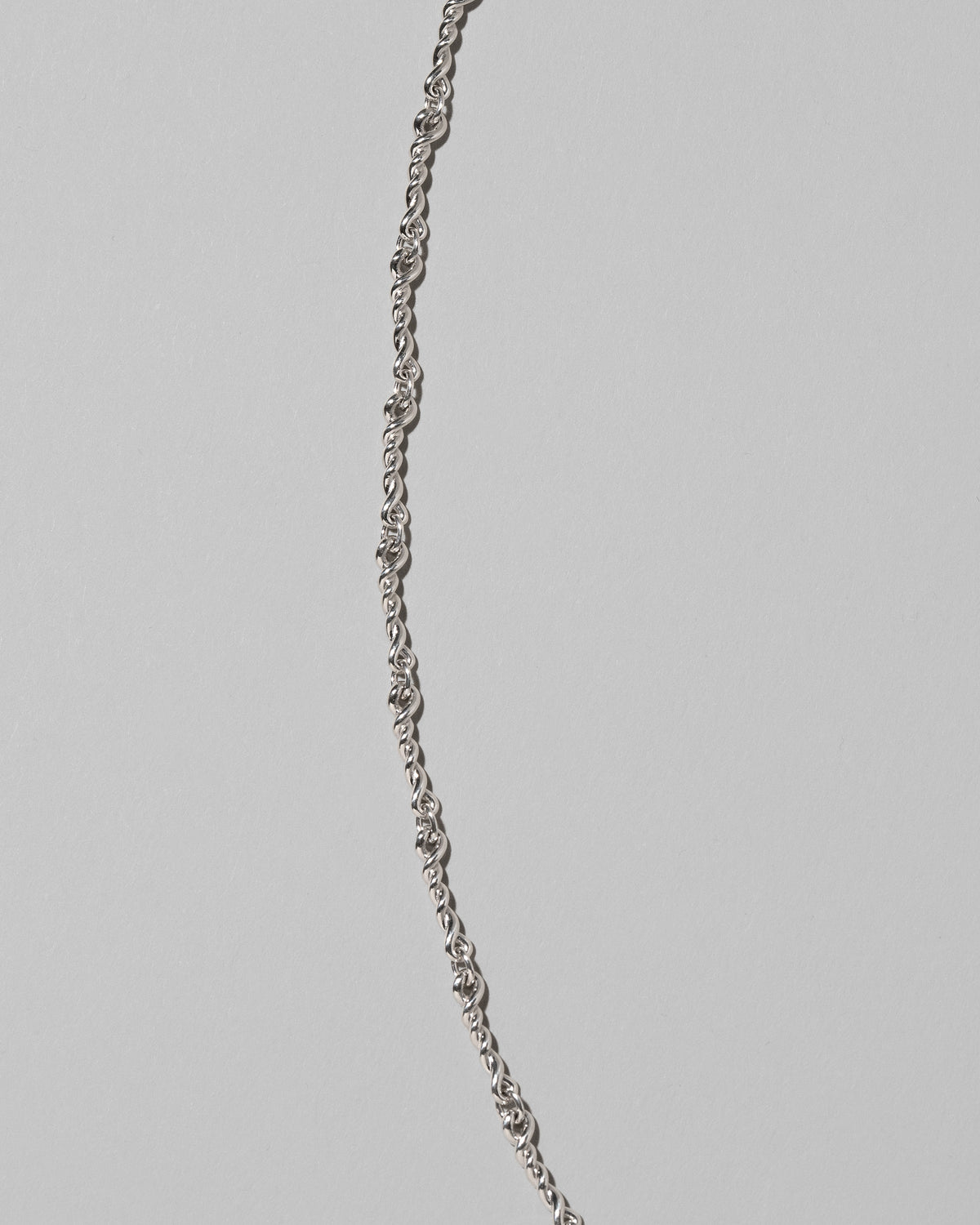 Closeup details of the CRZM Sterling Silver Double Helix Chain Necklace on light color background.