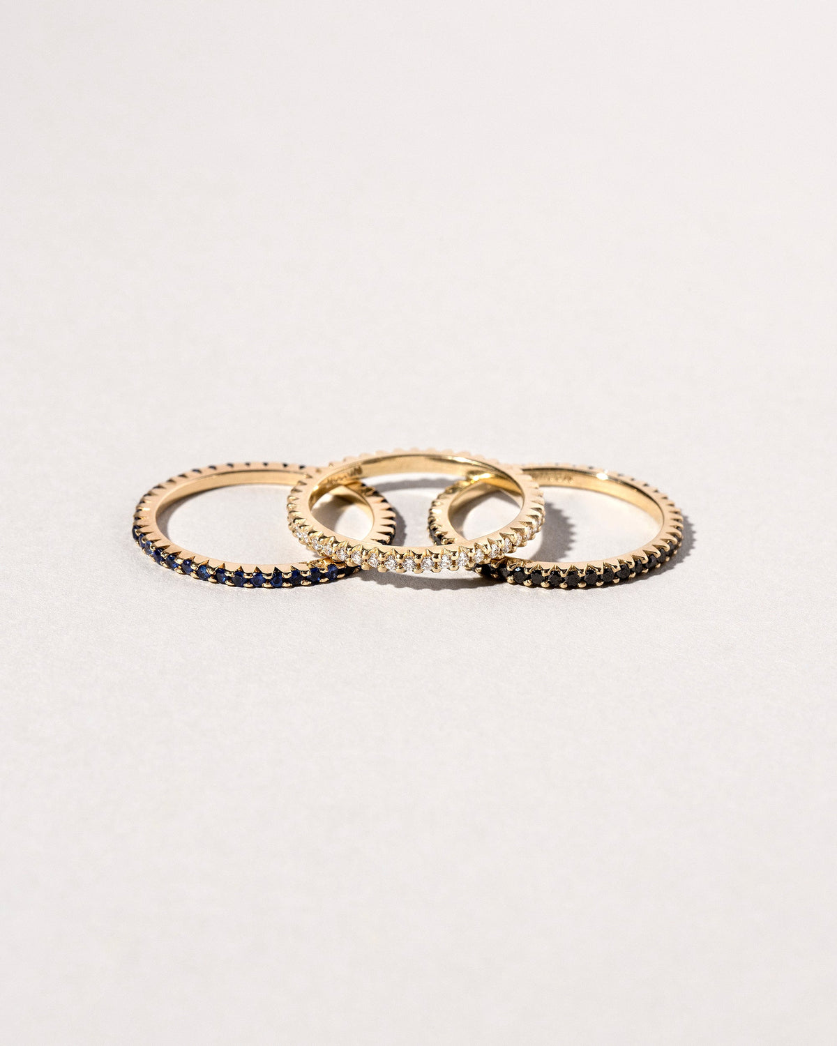 Gold Blue Sapphire Gear Edge Band, Gold White Diamond Gear Edge Band and Gold Black Diamond Gear Edge Band on light color background.