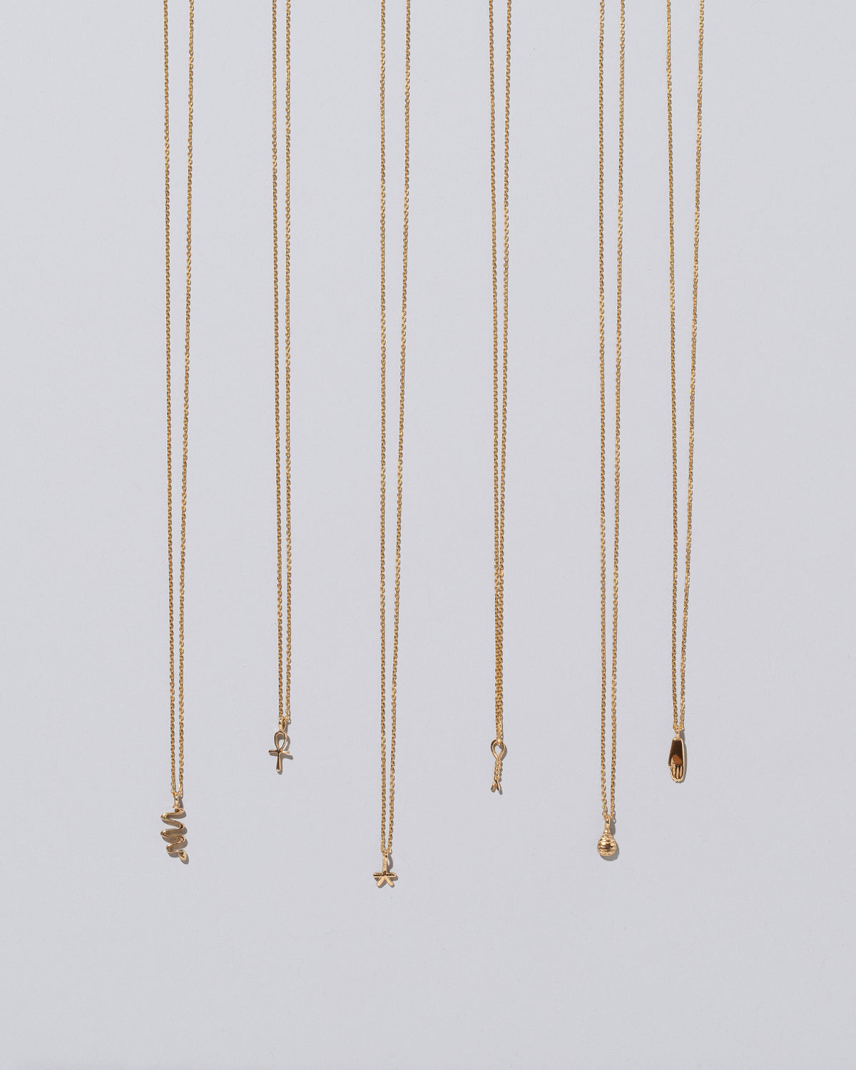 Group of Ankh, Star, Twist, Tear, Hand and Snake Talisman Pendant Necklaces on light color background.