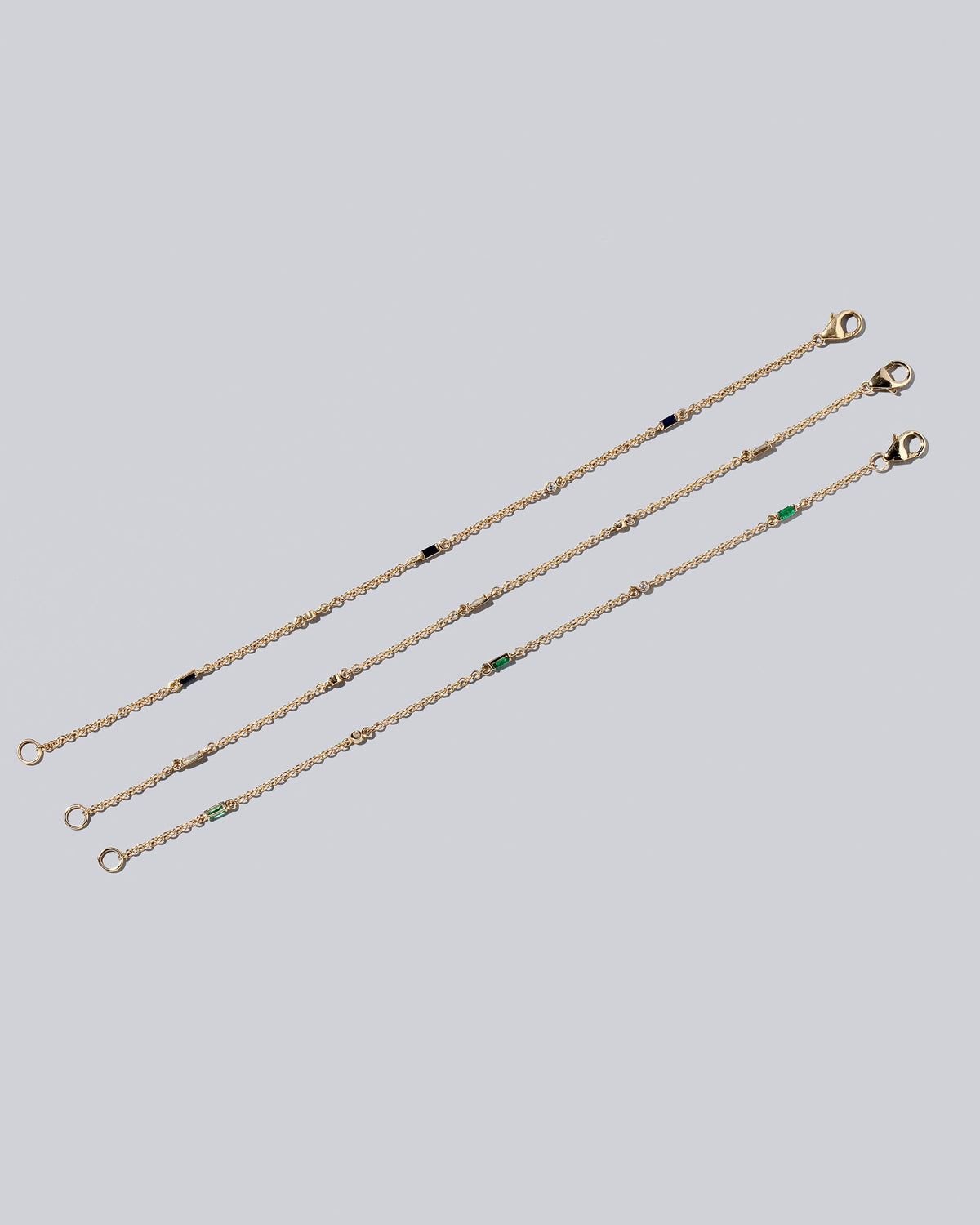 Group of Blue Sapphire, White Diamond and Emerald Distributed Building Blocks Bracelets on light color background.