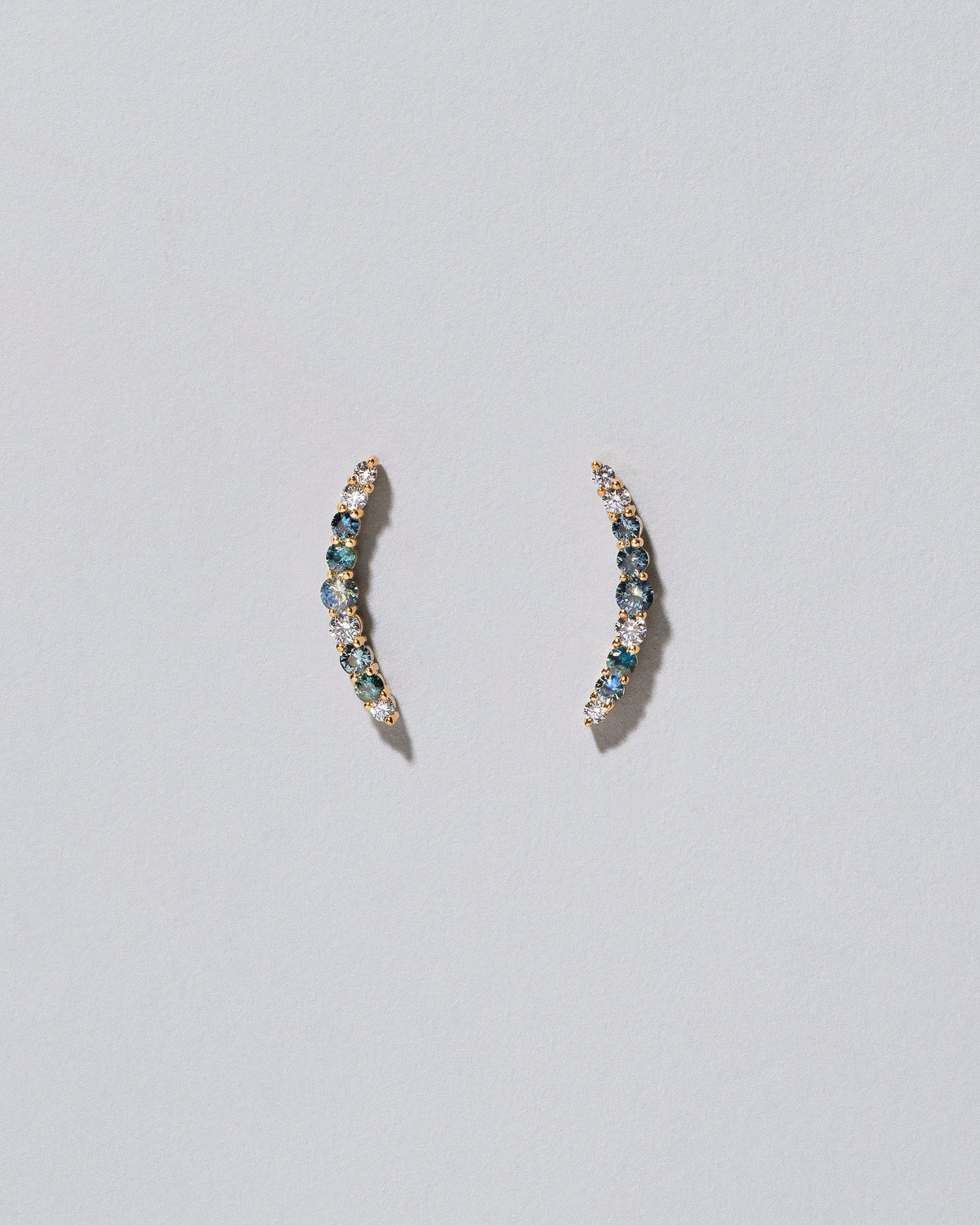 An edition of the Sapphire & White Diamond Crescent Ear Climber Stud Earrings on light colored background.