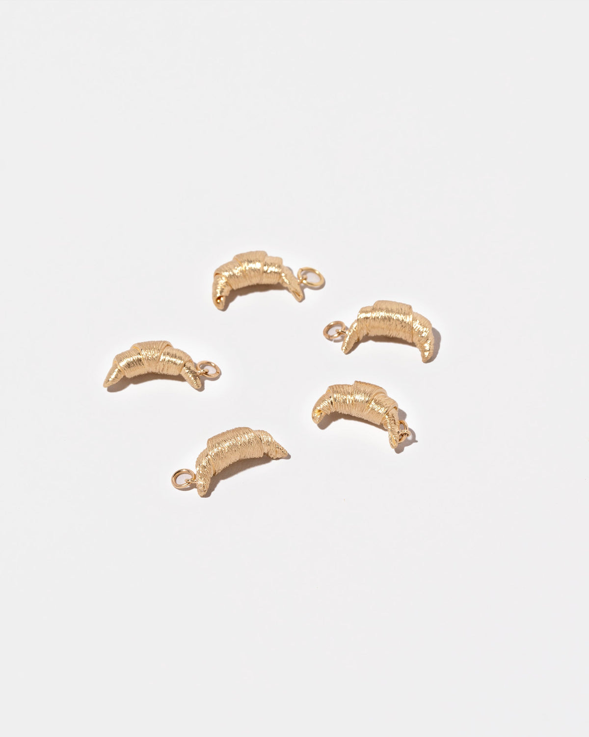 Group of Croissant Charms on light color background.