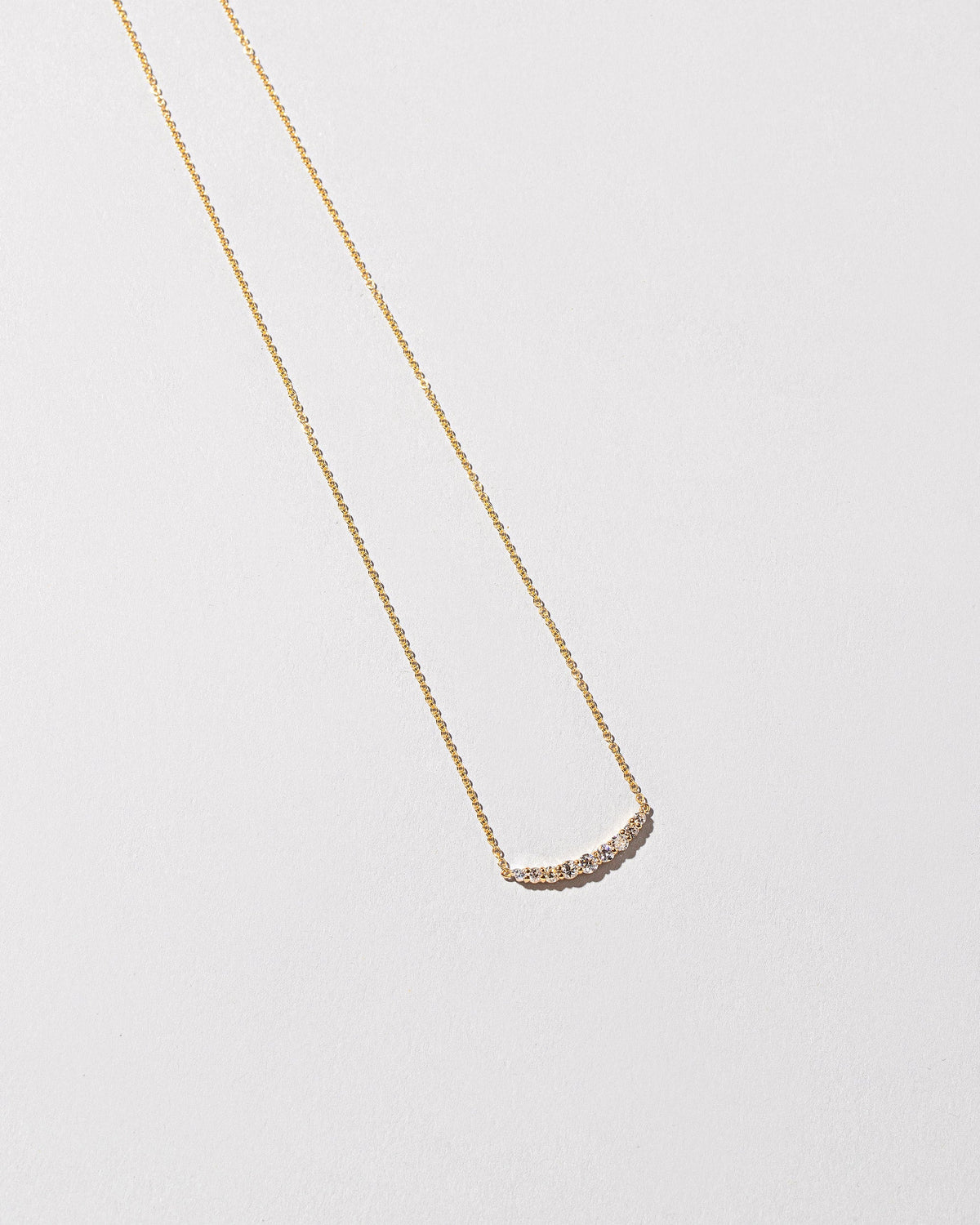 Closeup detail of the White Diamond Crescent Necklace on light color background.