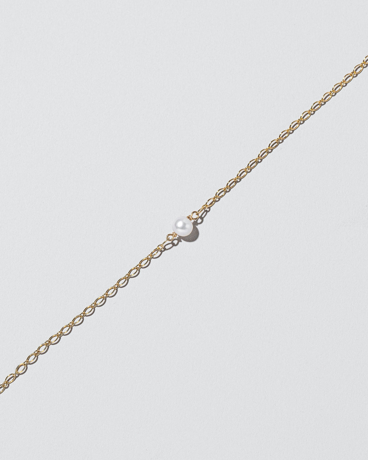 Closeup details of the One Pearl Station Bracelet Open Oval Chain on light color background.