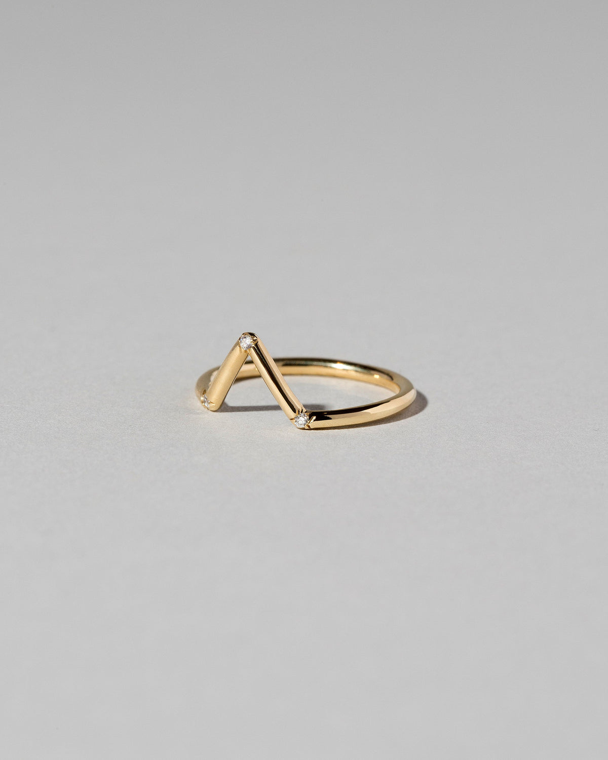 View from the side of the Gold White Diamond Three Stone Triangle Band on light color background.