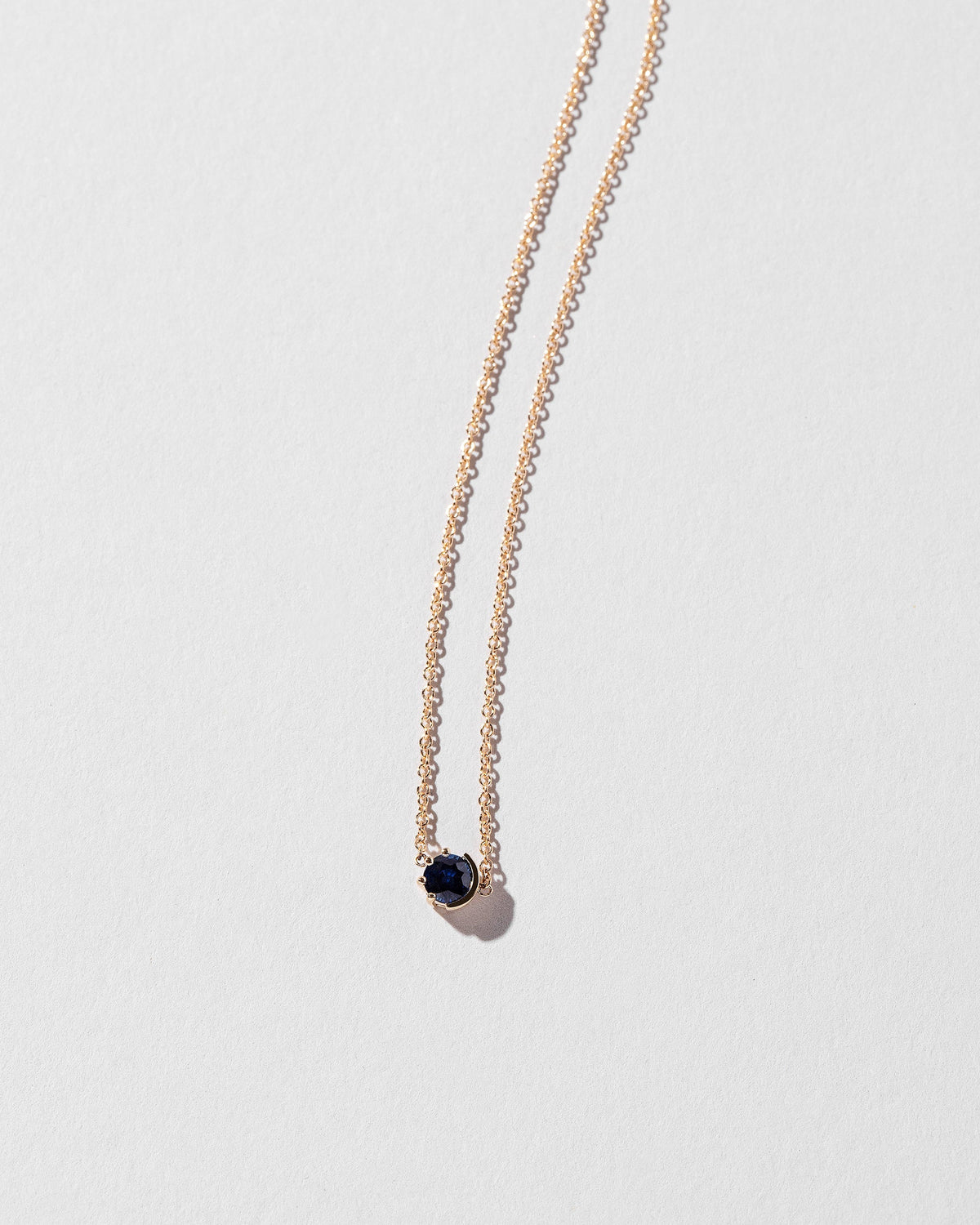 Closeup view of the Sapphire Sun & Moon Necklace on light color background.
