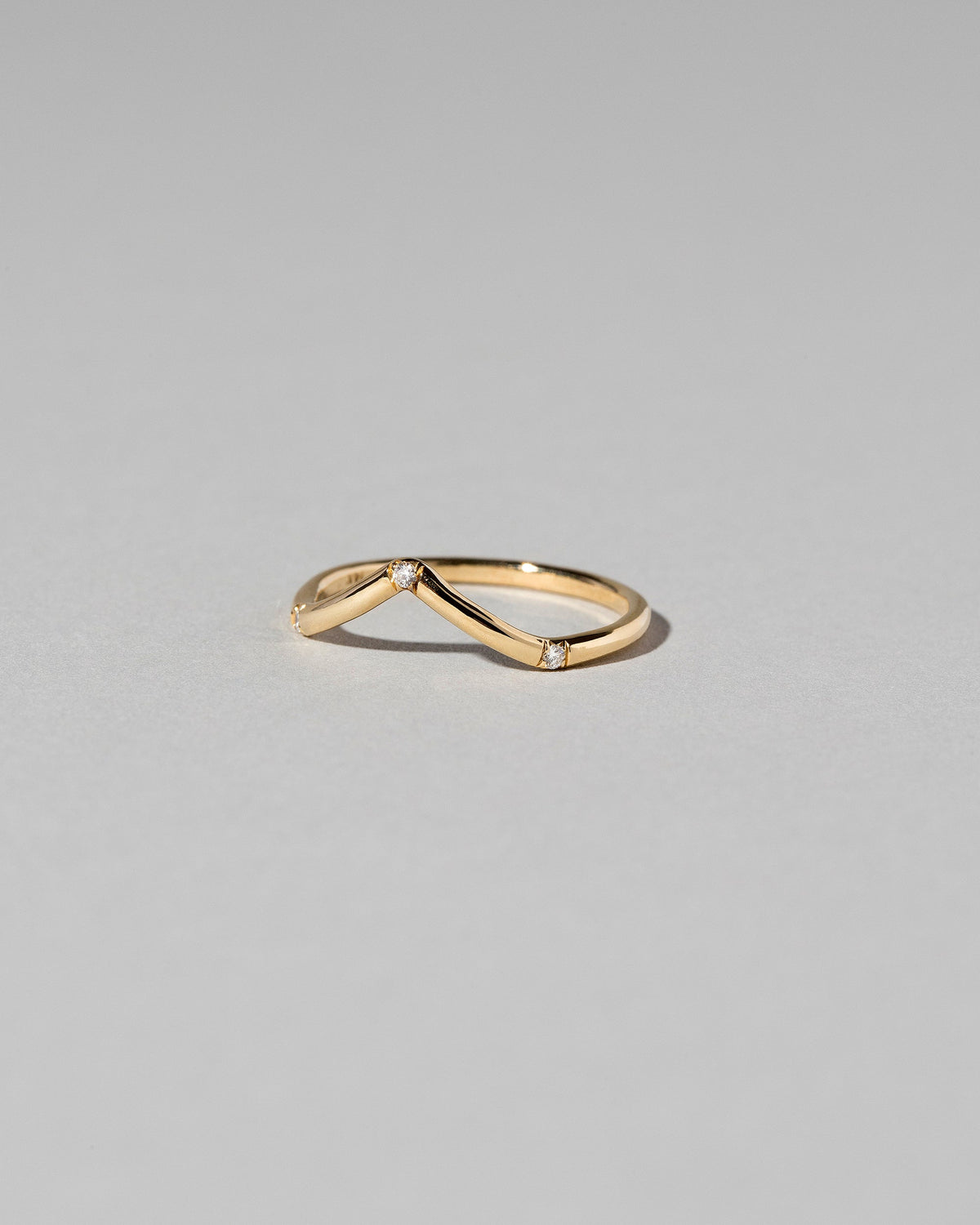 View from the side of the Gold Three Stone White Diamond High Peak Band on light color background.