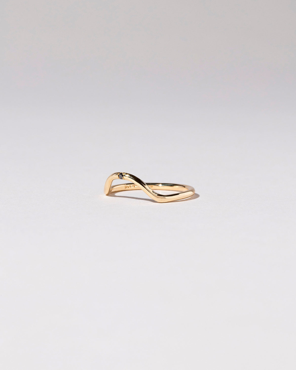 View from the side of the Gold Single Stone Black Diamond Curve Band on light color background.