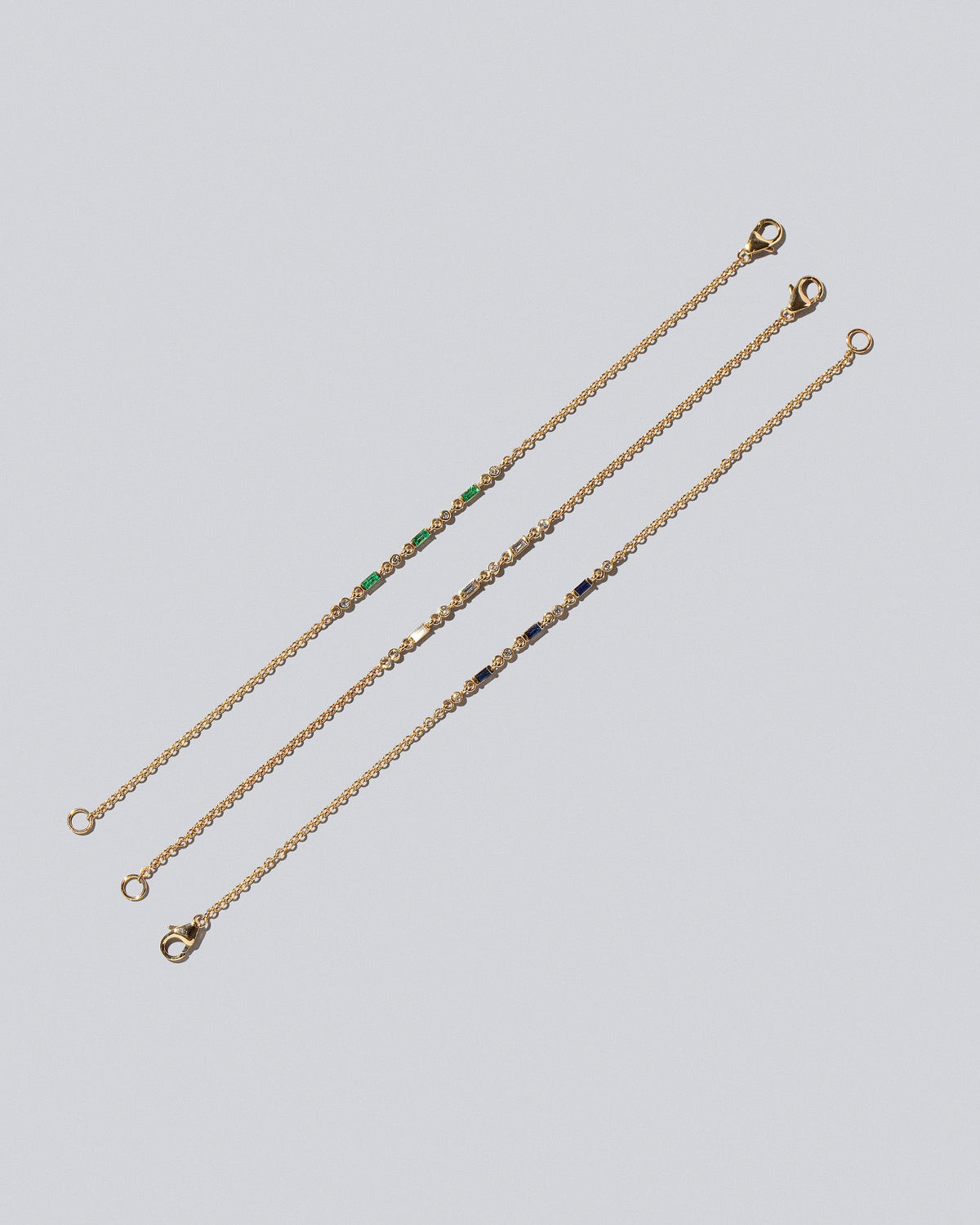Group of White Diamond, Blue Sapphire and Emerald Consecutive Building Blocks Bracelets on light color background.