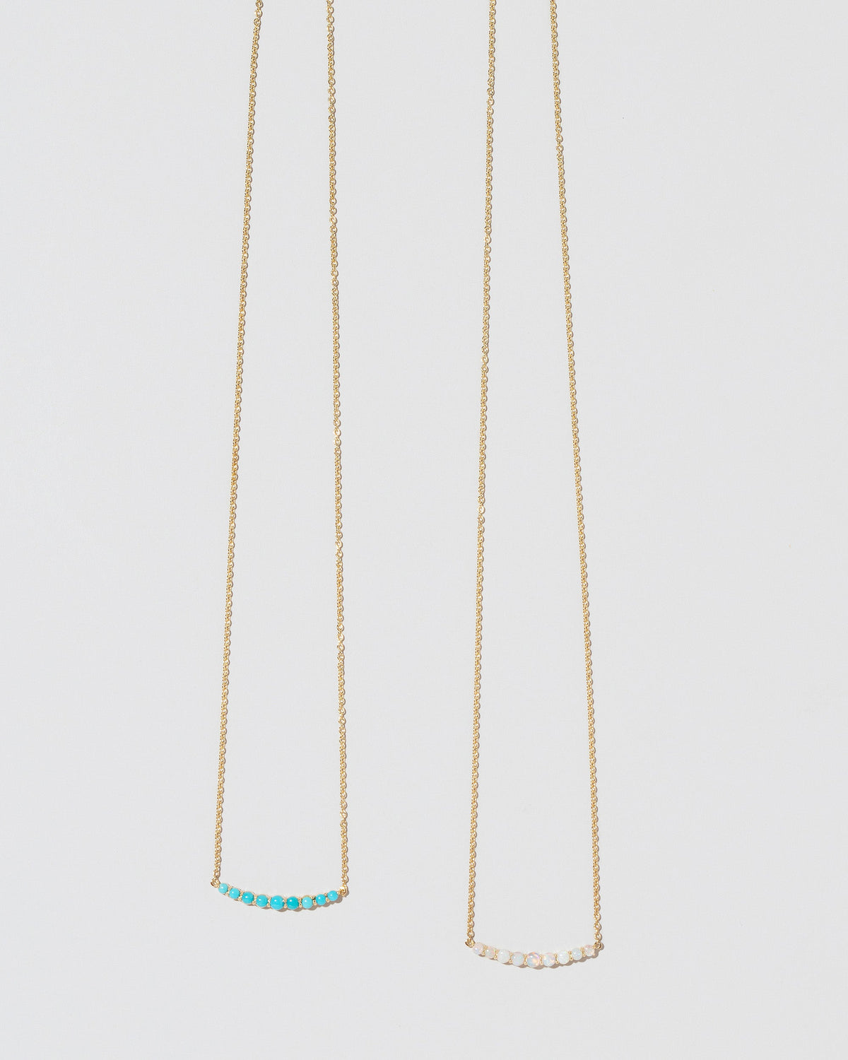 Closeup detail of the Opal Crescent Necklace and Turquoise Crescent Necklace on light color background.