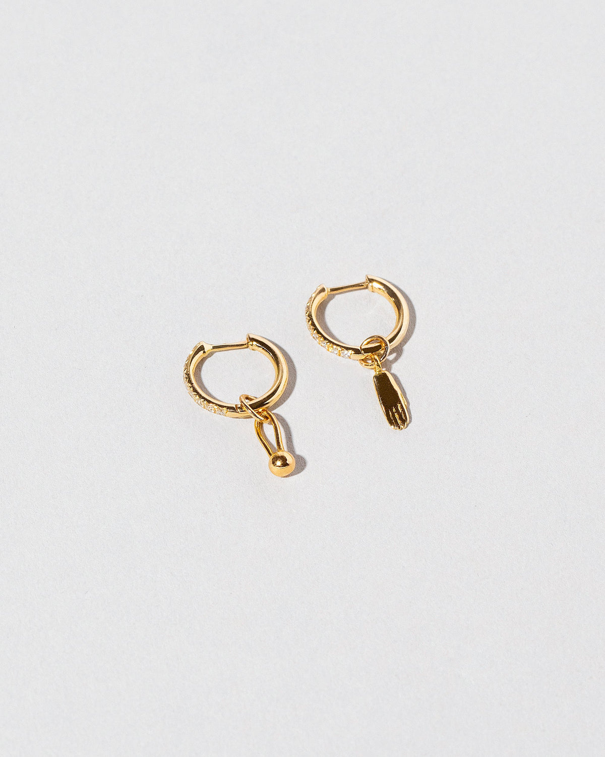 Gold Classic Diamond Snack Hoop Earrings with the Hand Talisman Charm and Loop & Sphere Talisman Charm on light color background.