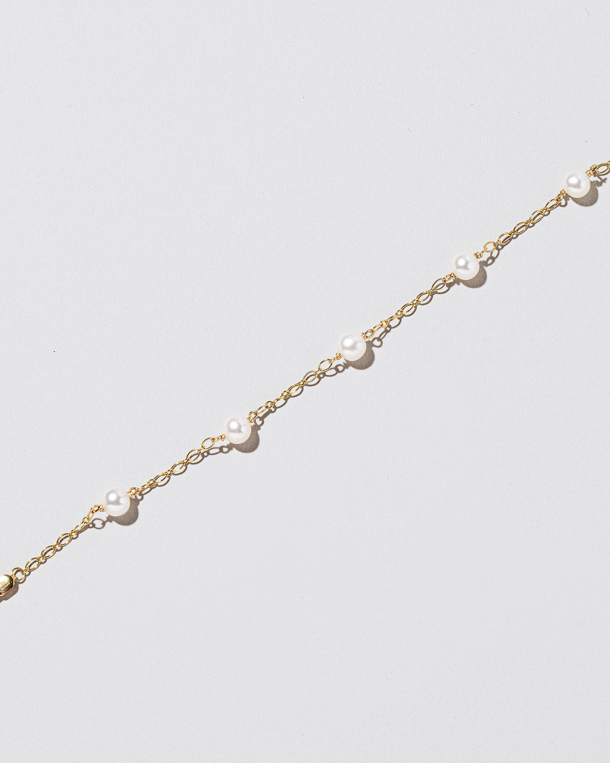 Closeup details of the Five Pearl Station Bracelet Open Oval Chain on light color background.