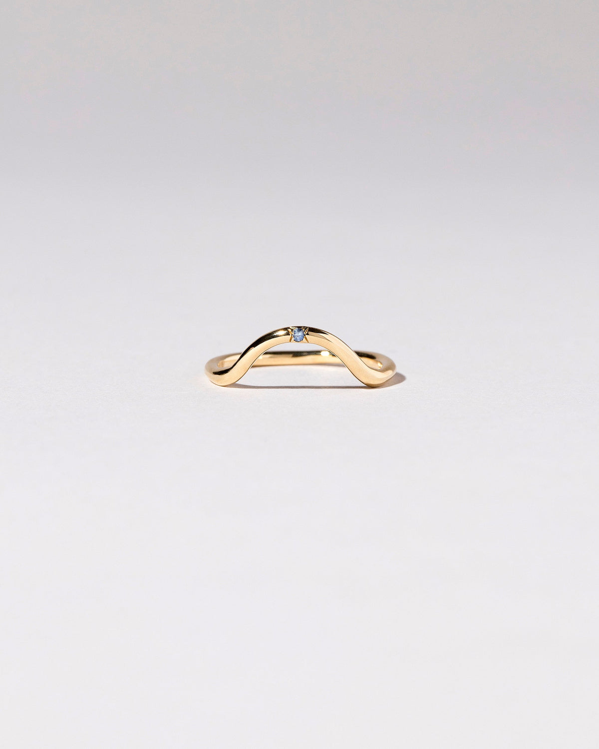Gold Single Stone Blue Sapphire Curve Band on light color background.
