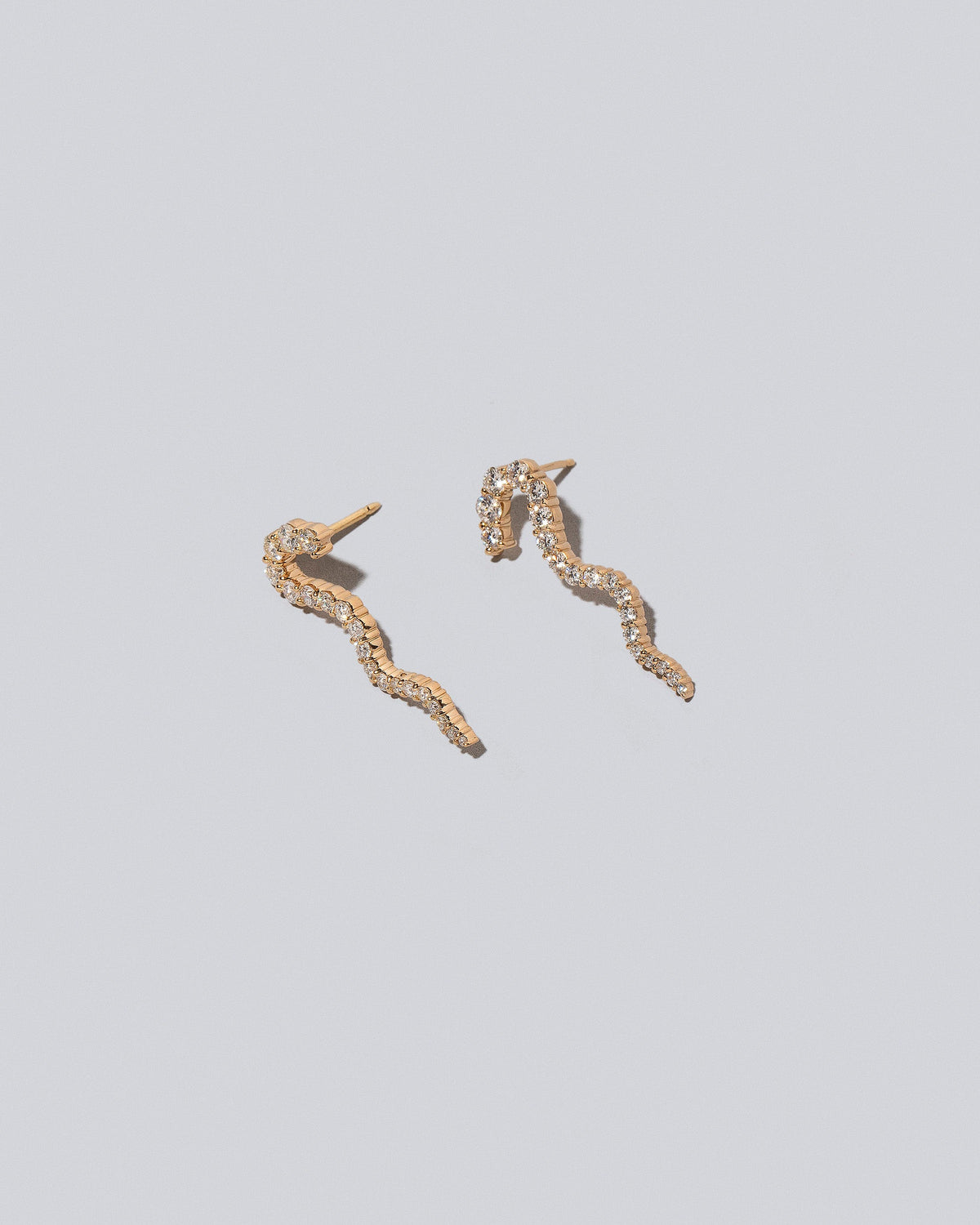 Closeup details of the Gold White Diamond Right Ripple Wave Earring Single and Gold White Diamond Left Ripple Wave Earring Single on light color background.